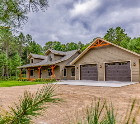 A modern two-story house with a large garage, wooden accents, and a porch, crafted by a skilled home builder in Eagle River, WI.