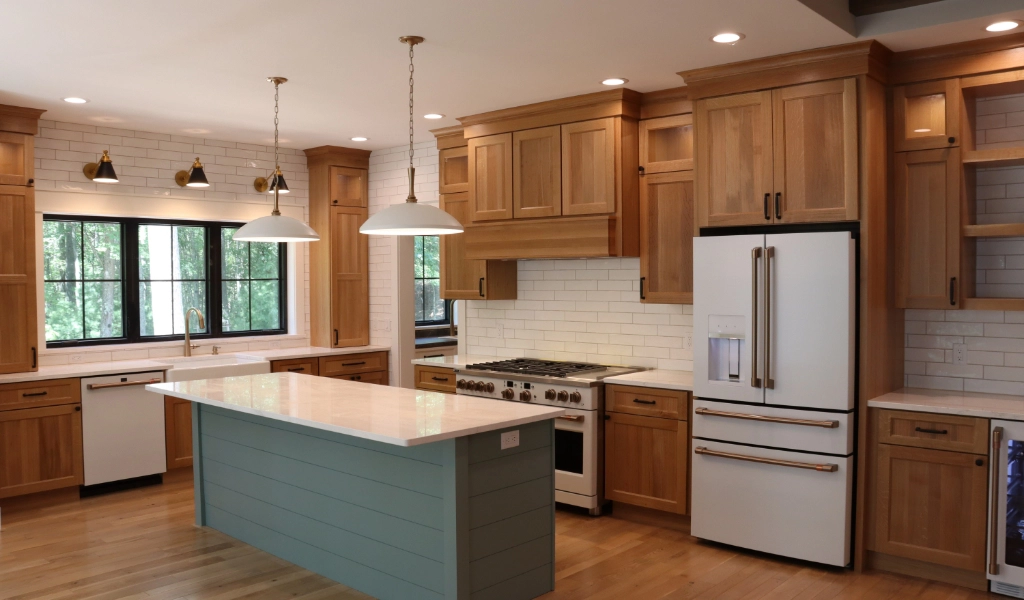 Spacious kitchen designed by a custom home builder, featuring wooden cabinets, white countertops, a central island, pendant lights, stainless steel appliances, and large windows.