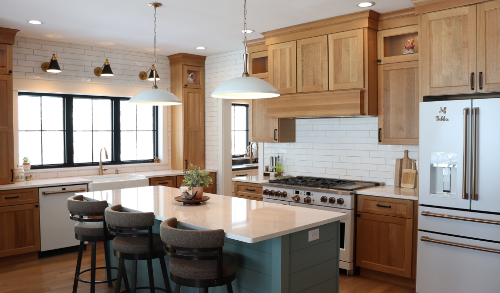 A modern kitchen features wooden cabinets, a blue island, stainless steel appliances, and white subway tile backsplash. Two pendant lights hang above the island, showcasing the craftsmanship of a custom home builder in Eagle River.