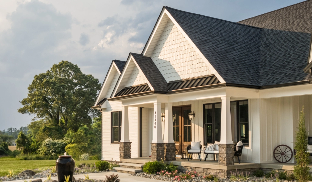 A modern custom home with a gable roof, front porch, and chairs welcomes visitors. The landscaped garden and large tree in the background showcase the exquisite craftsmanship of an Eagle River custom home builder.