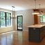 Modern kitchen and dining area with large Pella Windows, light wood flooring, a central island with drawers, pendant lighting, and a black-framed glass door leading outside.