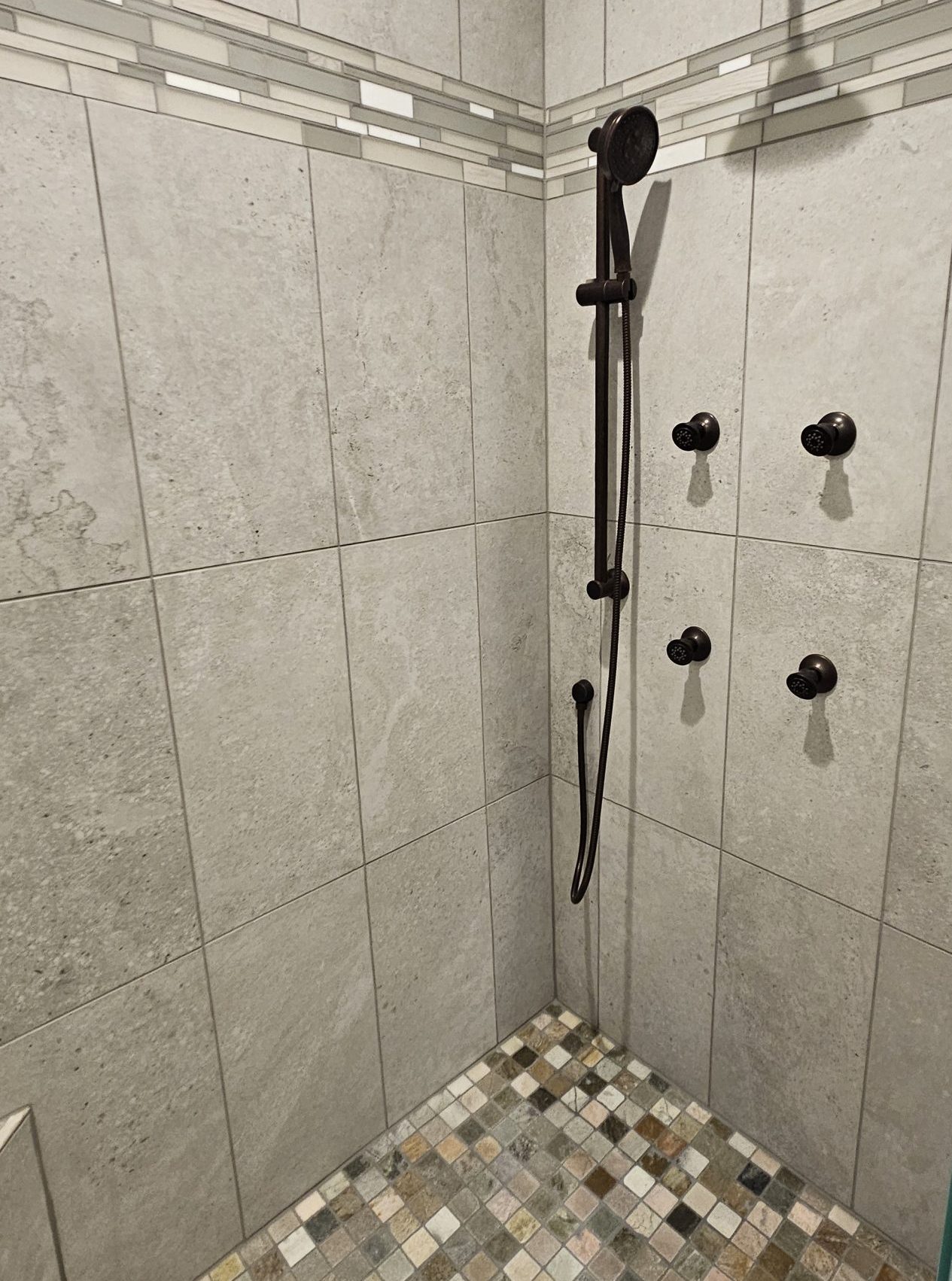 Modern tiled shower with a rainfall shower head, handheld shower, three wall-mounted controls, and a floor of small square mosaic tiles—perfect inspiration for tile pattern selections in your new home.