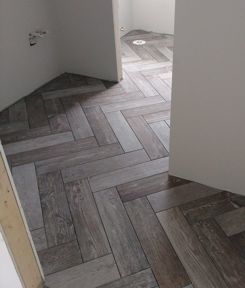 A room in a new home features unfinished white walls and a floor covered in dark wood-look tiles arranged in a herringbone pattern, showcasing stylish tile pattern selections.