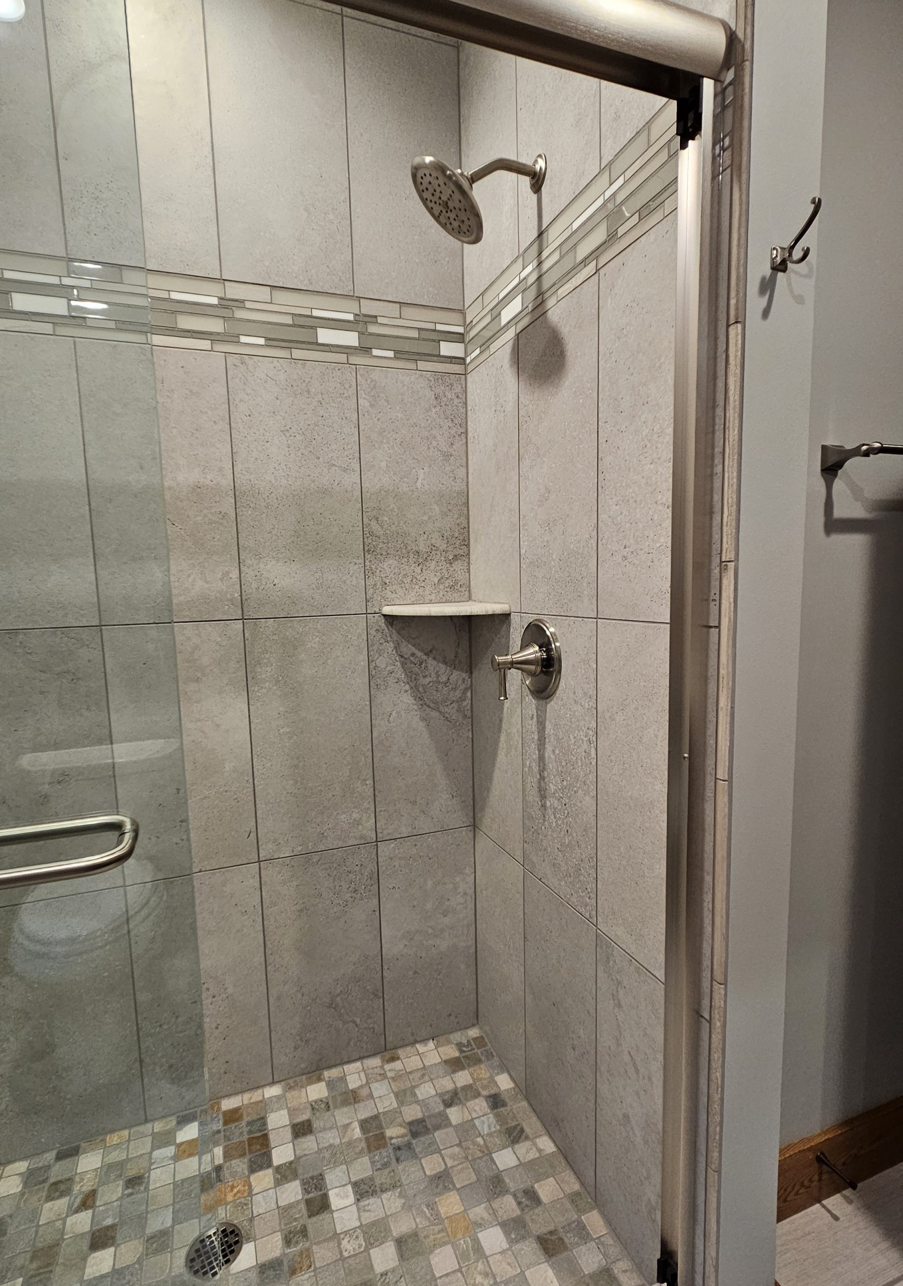 A tiled walk-in shower with a wall-mounted showerhead, a built-in corner shelf, and a metal grab bar along the left wall showcases thoughtful tile layout for your new home.