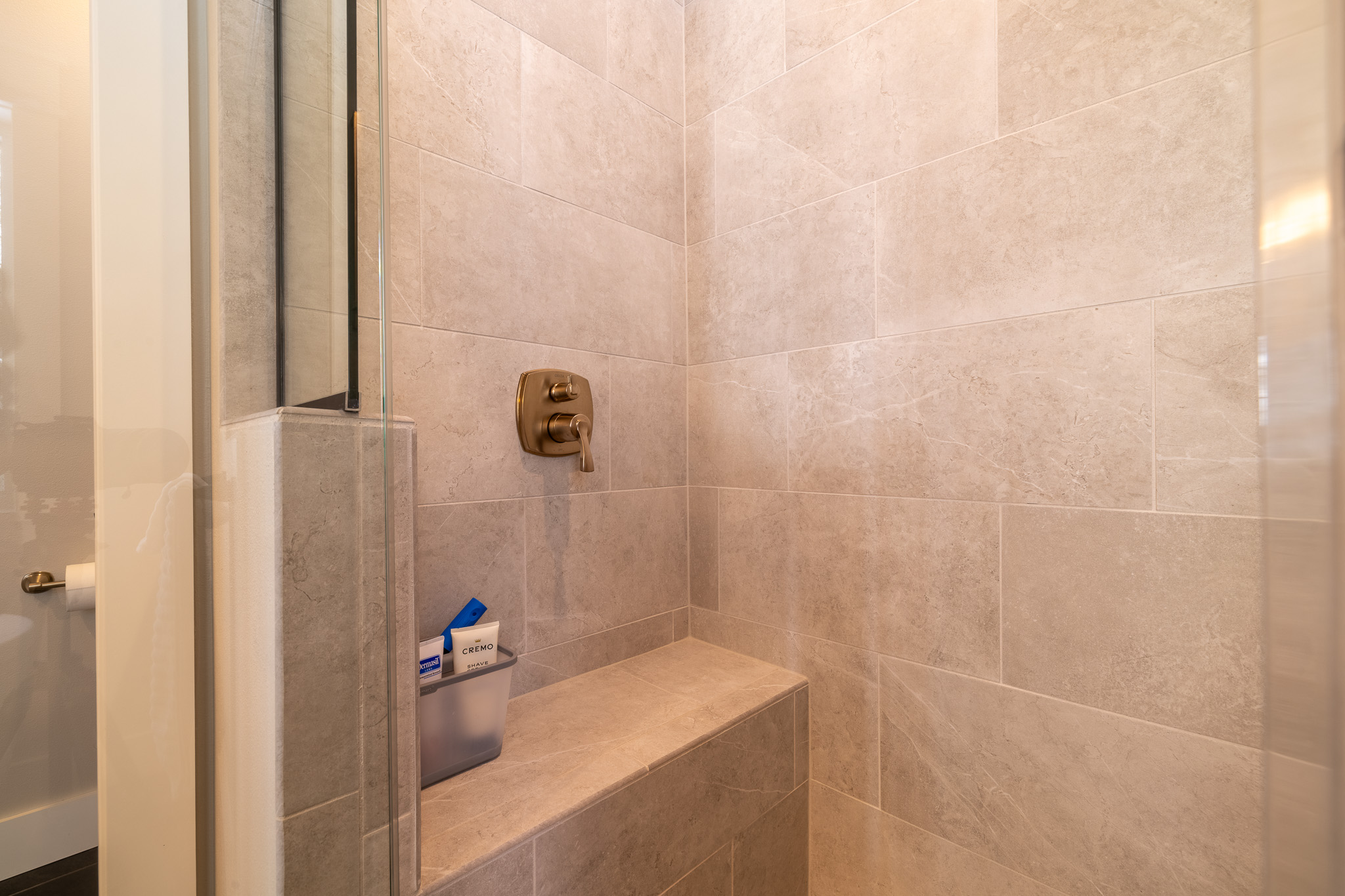 A tiled shower with a built-in bench, a wall-mounted shower control, and a frosted organizer holding bath products highlights the elegance of custom tile showers.