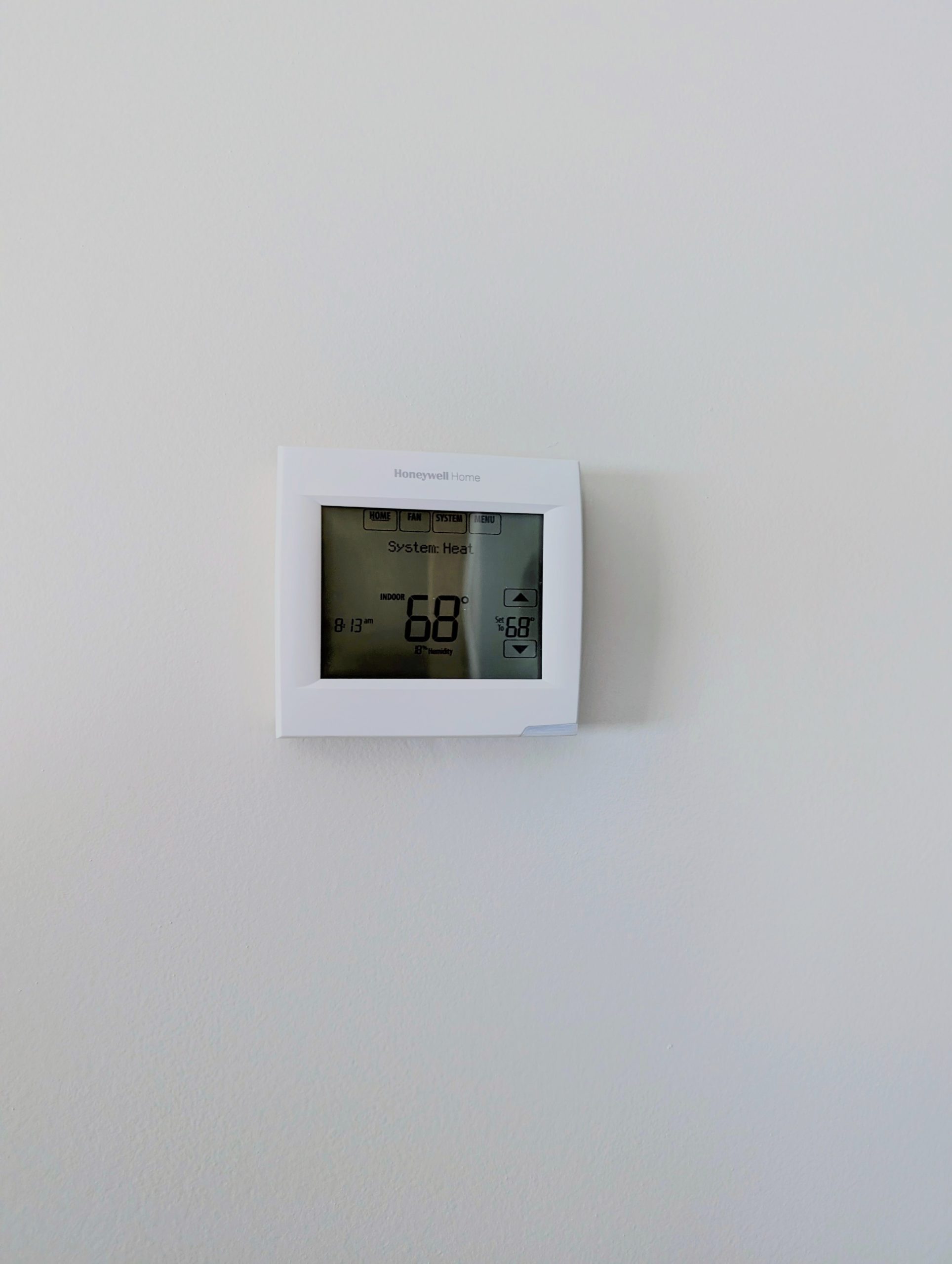 A digital thermostat mounted on a white wall displays the temperature set to 68 degrees, adding comfort and control to homes featuring custom tile showers.