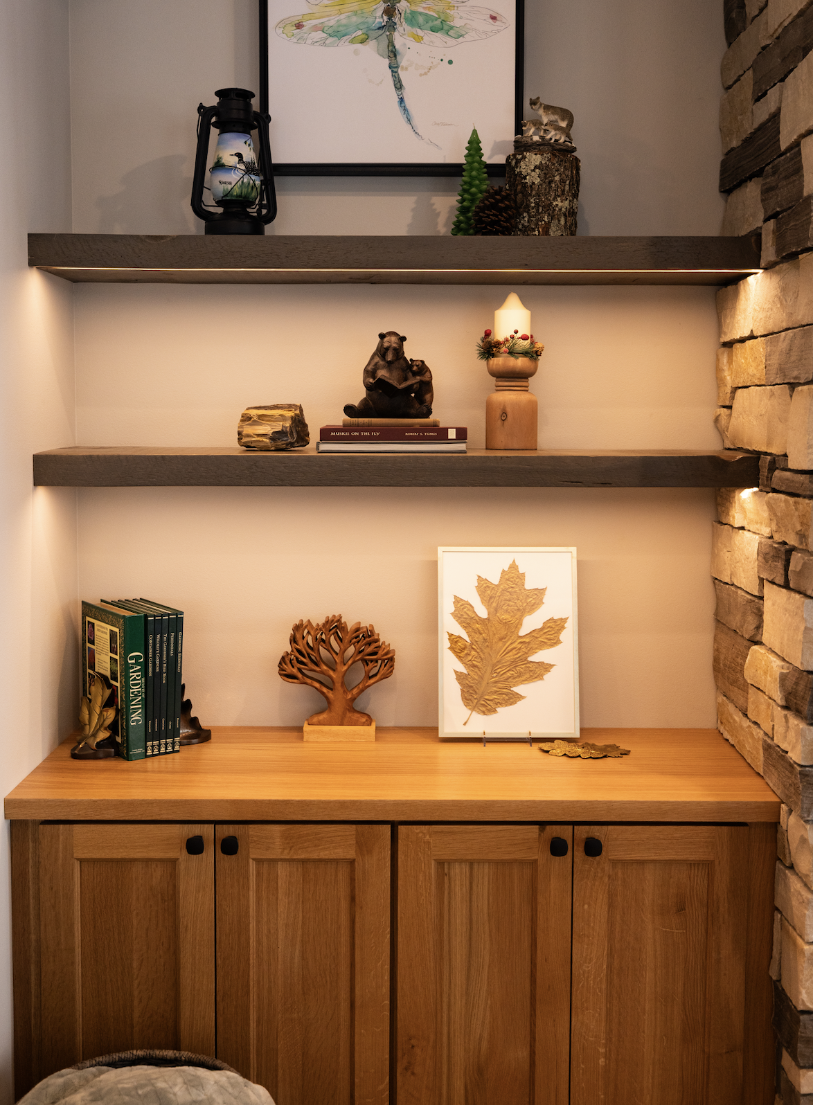 Wooden shelves with nature-themed decor, including a lantern, animal figurines, framed art, and a stack of books, illuminated by warm lighting above a wooden cabinet—perfect beside luxurious custom tile showers.