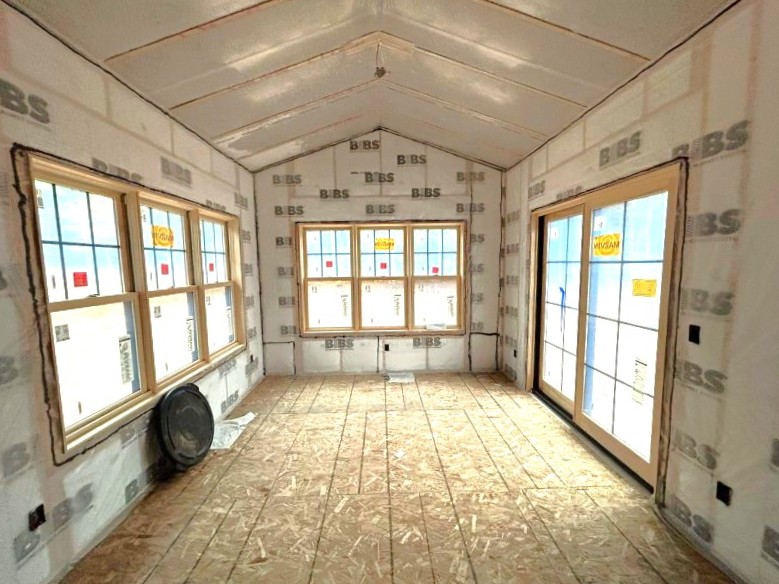 Unfinished room under construction with exposed insulation, three windows on one wall, a set of glass doors on the adjacent wall, and space ideal for custom tile showers.