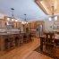 Spacious kitchen and dining area with wooden cabinets, center island with bar stools, stainless steel appliances, and a rectangular dining table on a patterned rug. Enjoy the home's custom tile showers for a touch of luxury.