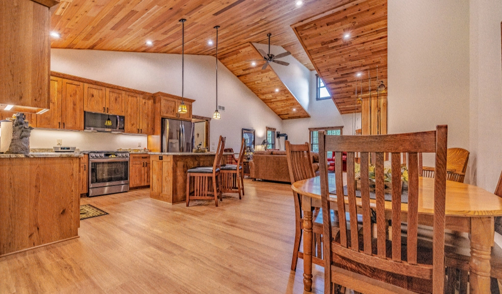 Open-concept kitchen, dining, and living area with wood floors, wooden furniture, vaulted wood-plank ceiling with recessed lighting and ceiling fans. Home also features stylish custom tile showers for a luxurious touch.